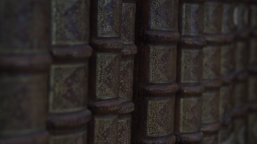 Stack of old leather bound books with a brass magnifying glass on top